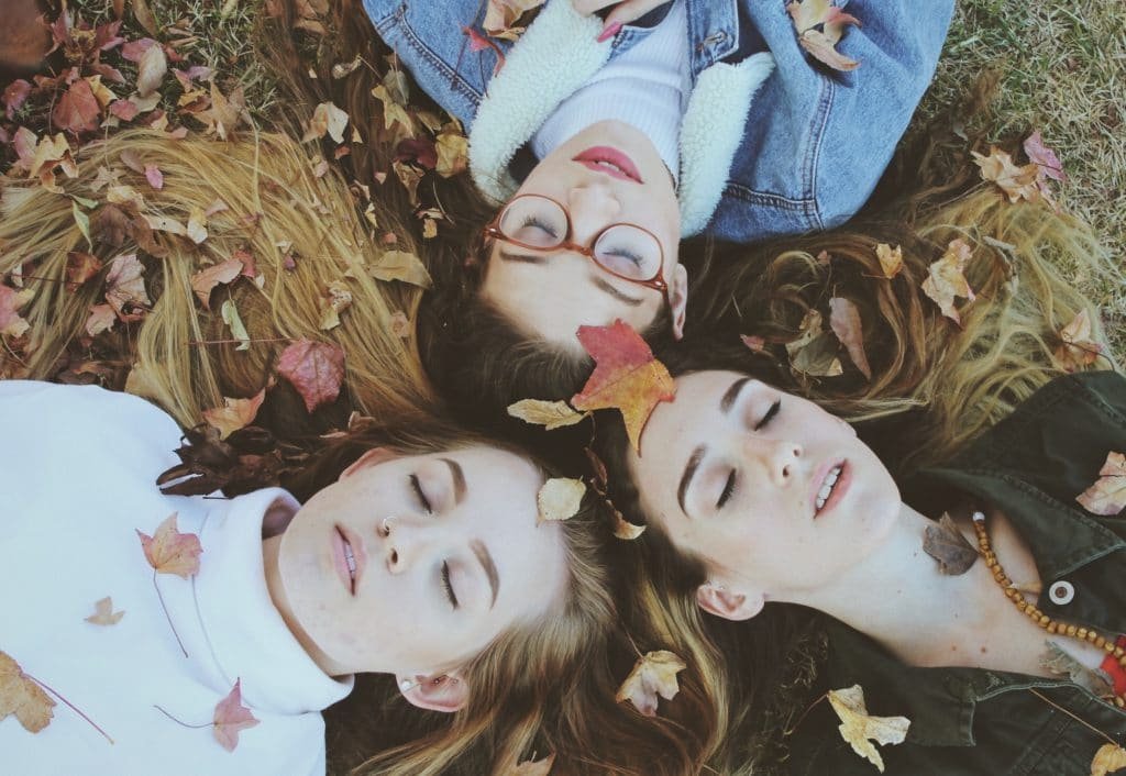 three girls on the grass enjoying autumn leaves falling on them